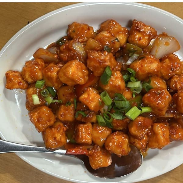 Chili Paneer, a popular Indian appetizer, with a spoon on a white plate.