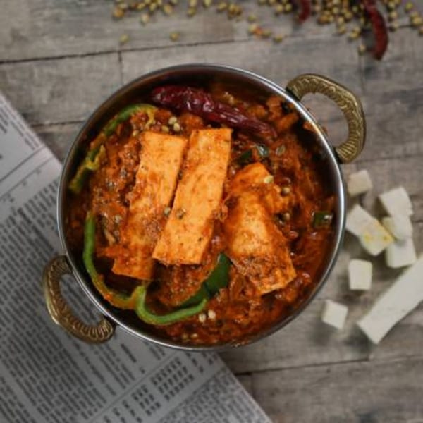 Kadhai Indian Cuisine's paneer dish in a metal bowl with green peppers and dried chilies.