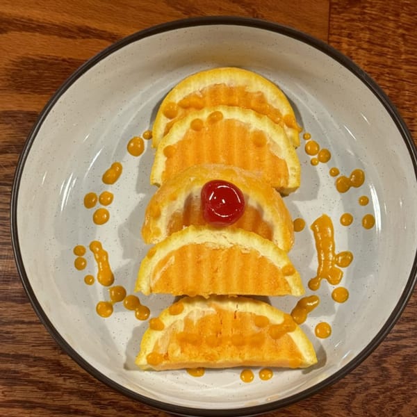 Four half-moon shaped Indian desserts with orange filling, garnished with a cherry and orange sauce.